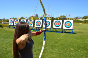 Female archer in field holding bow and arrow and getting ready to shoot target off in the distance