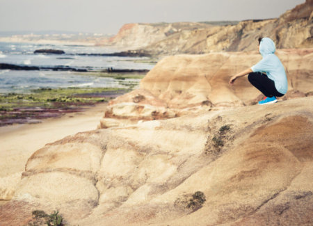 Woman wearing athletic wear and running shoes sitting on top of a cliff looking out into the ocean after a run